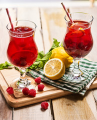 On wooden boards are two ice cold beverage glasses with red raspberry lemon cocktail . Alcohol country cocktail beverage number two hundred and seven with checkered cloth. Top view cocktail .