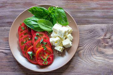 Ripe tomatoes, feta cheese and basil leaves on wooden table.