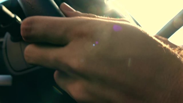 Man putting his hands on leather steering wheel against blazing sun, warm colors. 4K video
