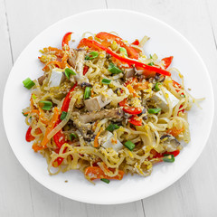 Plate of stirred rice noodles with tofu, vegetables and shiitake on a table. Traditional Asian cuisine meal. Top view.
