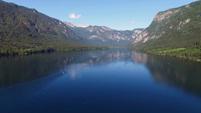 4K. Flight above amazing Bohinj Lake in the morning. People are training in rowing. Blue deep water and Julian Alps mountains. Triglav National Park, Slovenia, Europe.