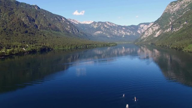 4K. Flight above amazing Bohinj Lake in the morning. People are training in rowing. Blue deep water and Julian Alps mountains. Triglav National Park, Slovenia, Europe.