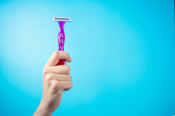 Red shaver in woman hand against blue background