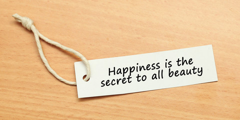 White tag on wooden background with word quotes of Happiness is the secret to all beauty