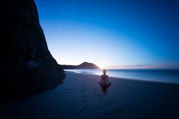 Silhouette young woman practicing yoga on the beach