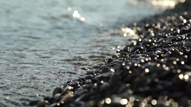 Close-up movie waves and drops lapping agains a pebble beach with shallow depth of field.
