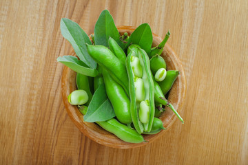 Green broad beans in a wooden bowl. Healthy raw vegetable on a table. Raw organic food.