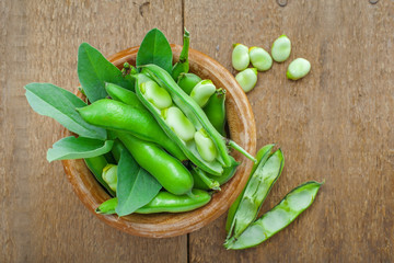 Bowl of fresh podded broad beans on a wooden table. Healthy organic food. Top view.