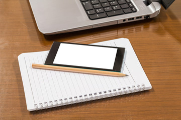 Blank notebook, pencil with smartphones and laptop on wooden table