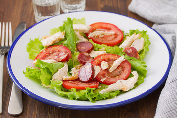 fresh salad with chicken and chourico on white dish on brown wooden background