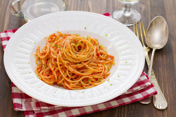 spaghetti with sauce and herbs on white plate and glass of white wine on brown wooden background