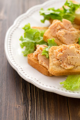 fish pate on toatst on white plate on brown wooden background