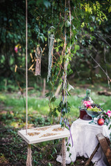 Old wooden swing hanging from a tree decorated with leaves on green grass background near still life