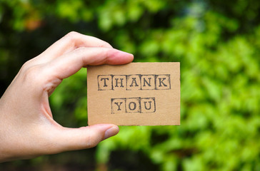 Woman hand holding cardboard card with words Thank You made by black alphabet stamps opposite green...
