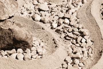 The texture of the stones and sand. Pattern of curved lines on the sandy beach amongst small pebbles. 