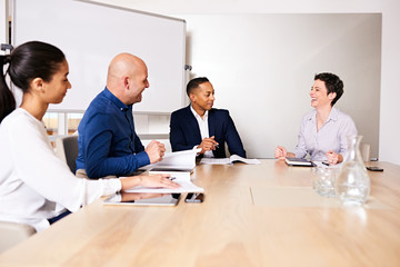 Business meeting between four elclectic partners as the mature white female laughs along with the other partners to a joke told by her colleauge to break the ice.