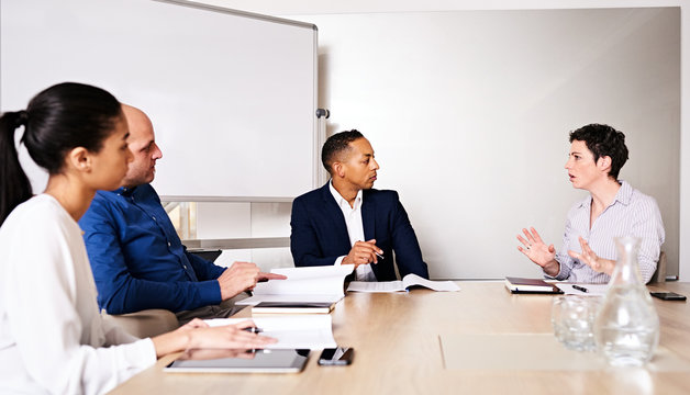 four young diverse business partners conducting a meeting in the board room of their new offices at the new conference table, with the mature caucasian female busy explaing her reasoning