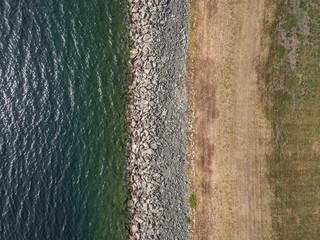 Birds eye view of a walking path alongside a body of water lined by rocks.