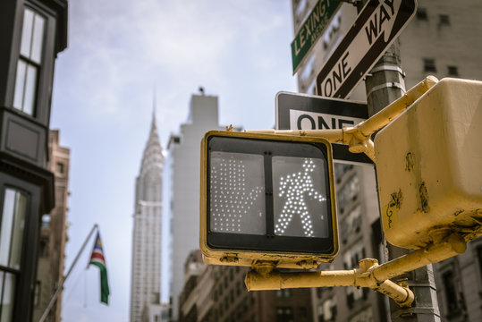 Yellow New York City crosswalk sign on busy one way street with skyline in the background.
