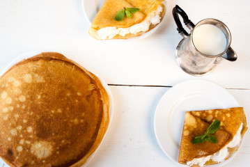 A light breakfast or lunch, with pancakes (crepes) and whipped cream. On the table is the coffee. Sunny morning, white wooden table