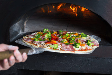 Chef puts pizza to the wood-fired oven which is very hot. He is transporting pastry at special...
