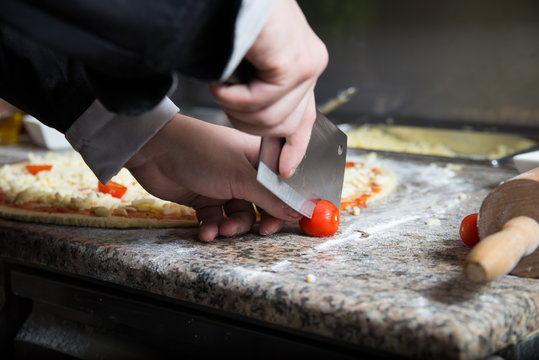 Man cuts fresh tomatoes by very sharp knife at the kitchen worktop. He is going to add this to vegetarian pizza. 