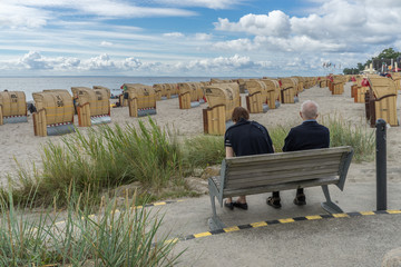 Ein älteres Paar blickt über Strandkörbe auf das blaue Meer
