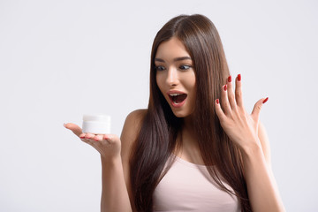 Cheerful girl staring at facial balm with surprise