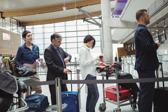 Passengers waiting in queue at a check-in counter with luggage