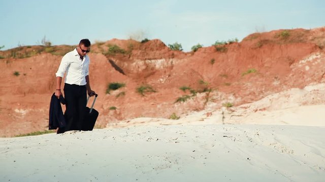 Businessman in desert. A young man in a business suit and a large luggage bag in the desert. Businessman on the road to the resort. White sand. Sultry desert.