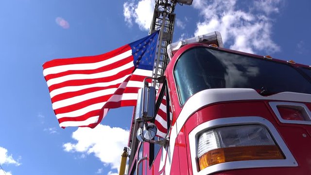 American flag waves in the wind from the ladder of a big red firetruck.