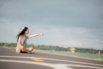 young woman sitting hitchhiking on a road with a suitcase
