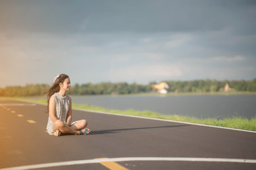 young woman sitting hitchhiking on a road with a suitcase