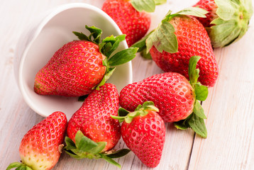 Fresh strawberries in white ceramic bowl on wood table