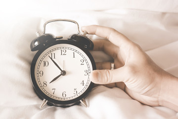 Alarm clock black style vintage place on a bed with hands of a man holding a clock.Vintage tone
