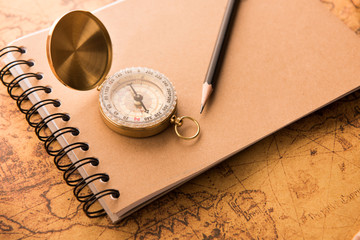 Fototapeta na wymiar Compass with note book and pencil on old map vintage style