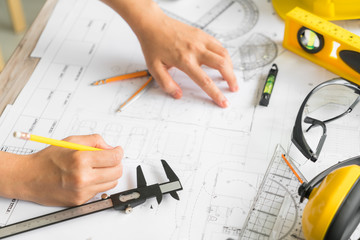 Hand over Construction plans with yellow helmet and drawing tool