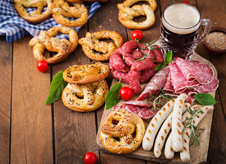 Glass of beer, pretzels and various sausages on wooden background. Oktoberfest. Top view
