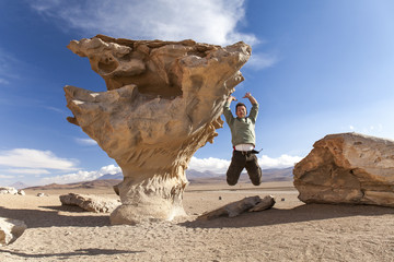 Young man jumping near the Stone tree, Bolivia ( Árbol de Piedra) Isolated rock in the desert. Mountain background