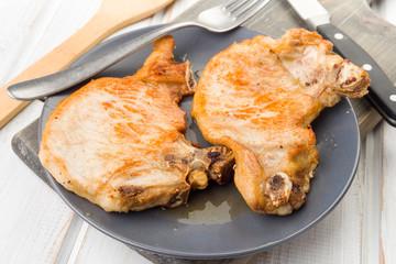 two chops roasted pork on plate, on wood