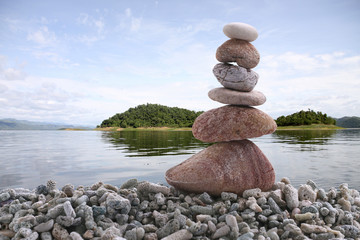 Balance stone on pile rock with river background.