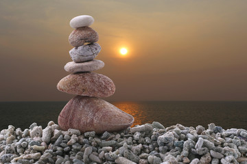 Balance stone on pile rock with sunset sea background.