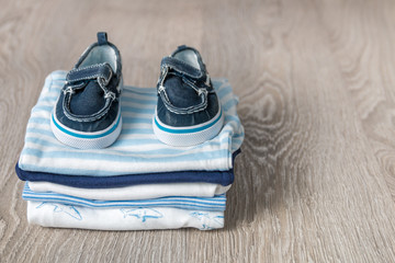 Folded blue and white bodysuit with shoes on it on grey wooden background. diaper for newborn boy....