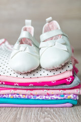 Fototapeta na wymiar Folded pink and white bodysuit with shoes on it on grey wooden background. diaper for newborn girl. Stack of infant clothing. Child outfit. Close up.