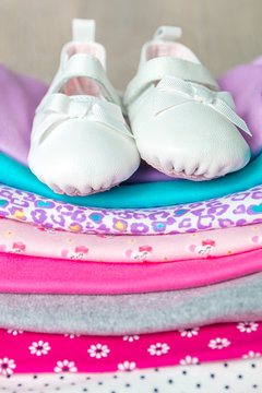 Folded pink and white bodysuit with shoes on it on grey wooden background. diaper for newborn girl. Stack of infant clothing. Child outfit. Close up.