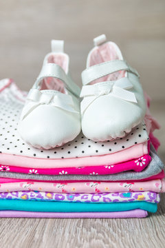 Folded pink and white bodysuit with shoes on it on grey wooden background. diaper for newborn girl. Stack of infant clothing. Child outfit. Close up.