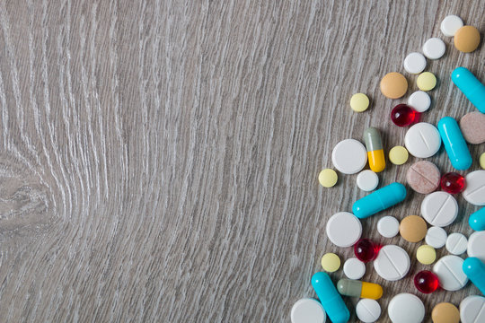 A lot of colorful medication and pills from above on grey wooden background. Copy space. Top view, frame. Painkillers, tablets, generic pills, drugs.