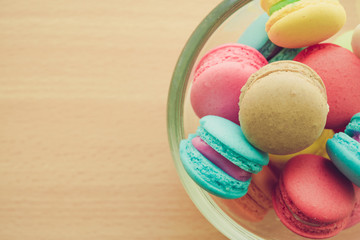 Colorful france macarons in glass cup on wooden background.