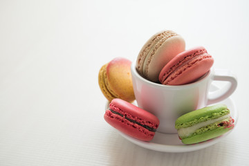 Colorful france macarons and cup on white wooden background.