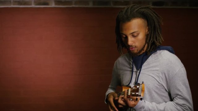 Handsome man with dreads plays a ukulele, in slow motion